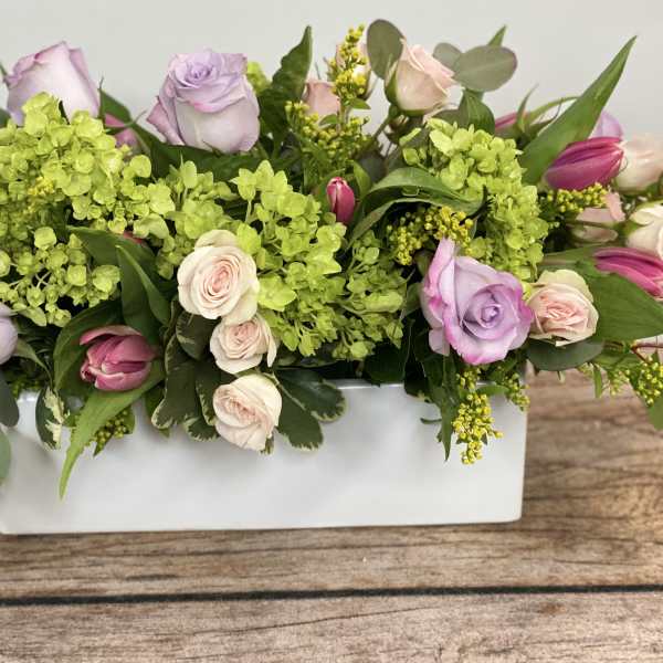 Rectangular floral arrangement with pastel roses and green hydrangeas in a white vase