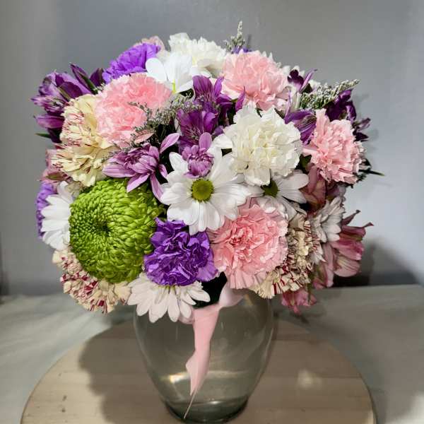 Mixed bouquet of pink, purple, white, and green flowers in a glass vase