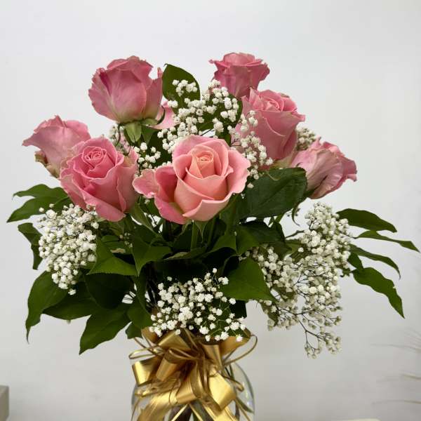 Pink roses in a glass vase with white baby's breath and a gold ribbon