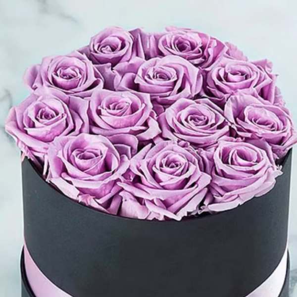 Lavender roses arranged in a black round box with a pink ribbon