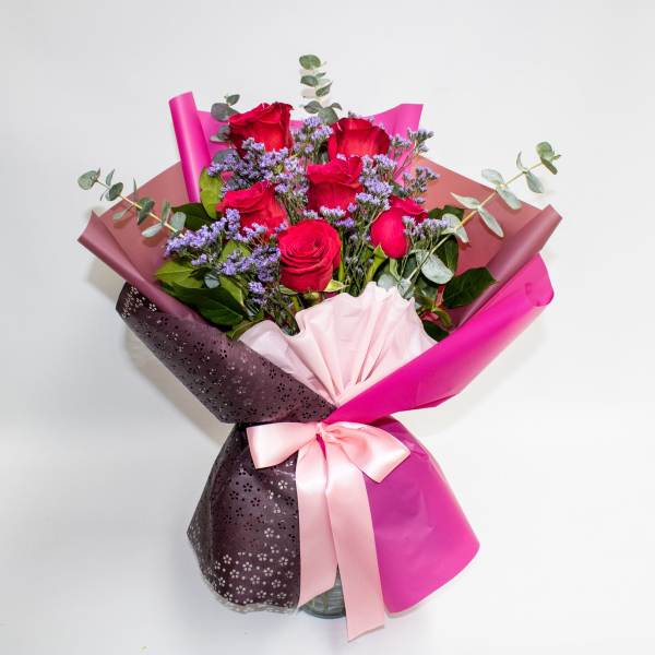 Bouquet of red roses with purple filler flowers wrapped in pink paper