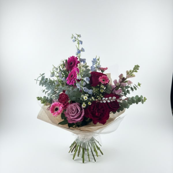 Bouquet of pink, purple, and blue flowers wrapped in beige paper