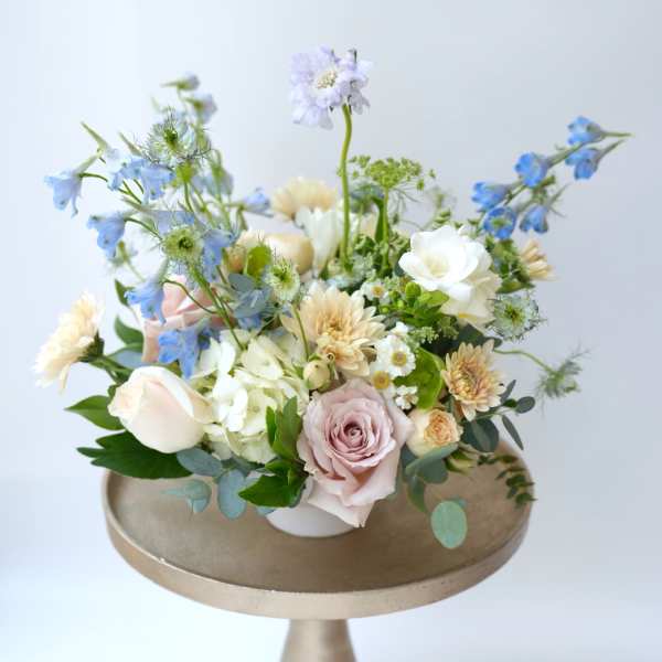 Pastel floral arrangement with roses, daisies, and blue blooms in a low vase