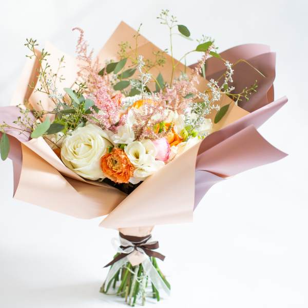 Bouquet of cream, peach, and pink flowers wrapped in pastel paper