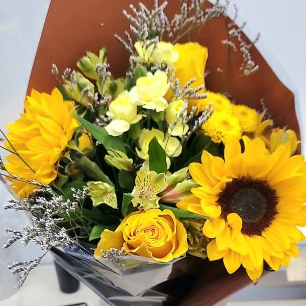 Bouquet of sunflowers, yellow roses, and pale yellow flowers in brown wrap