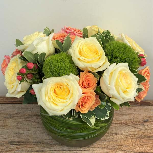 Cream and peach roses arranged in a round glass vase