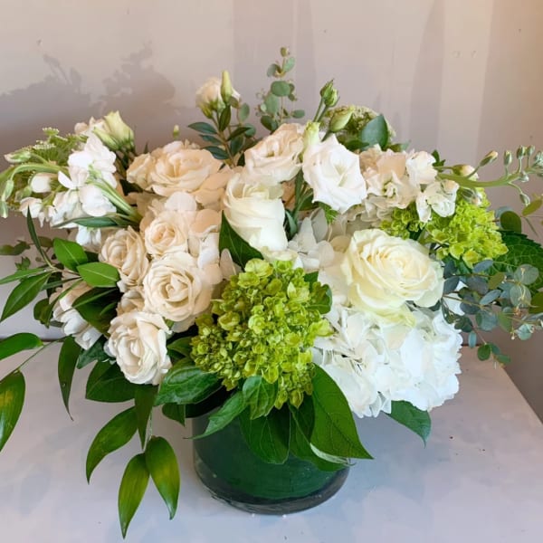 White and cream floral arrangement in a green vase with green accents