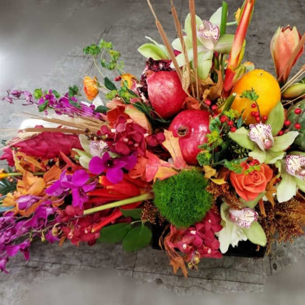 Colorful tropical floral arrangement with fruit in a low container