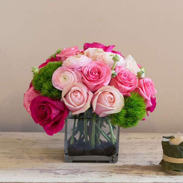 Pink and white roses arranged in a square glass vase.