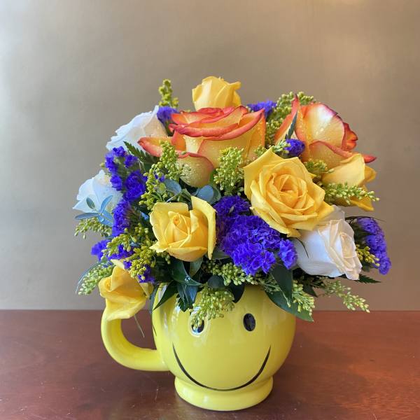 Bouquet of yellow, white, and orange roses in a yellow smiley-face mug