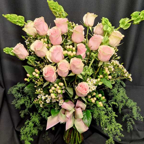 Pink roses arranged in a glass vase with greenery and a pink ribbon