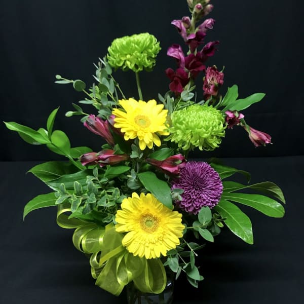 Mixed bouquet with yellow gerbera daisies, green chrysanthemums, and purple blooms in a vase