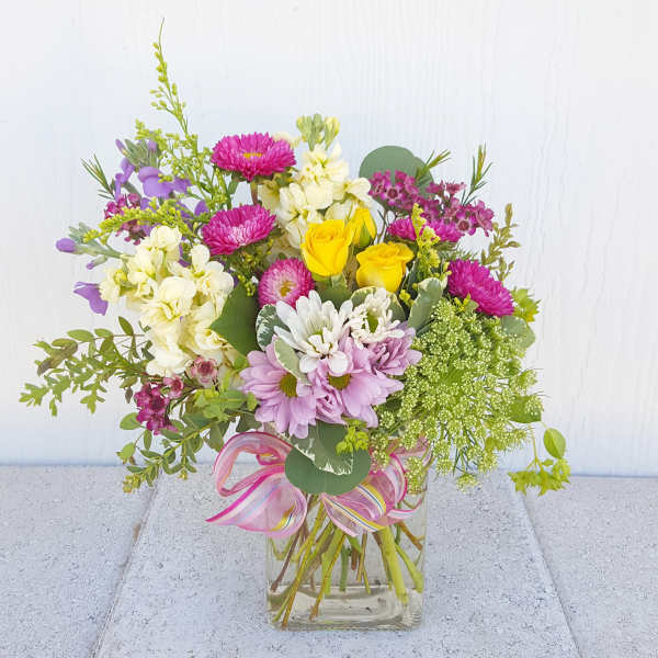 Mixed bouquet of pink, yellow, white, and purple flowers in a glass vase