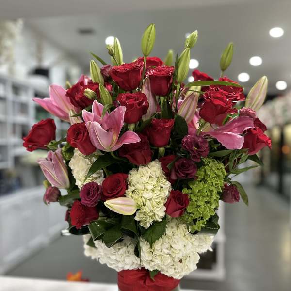 Bouquet of red roses, pink lilies, and white hydrangeas in a green vase