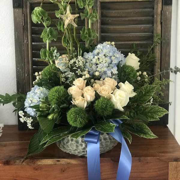 Blue hydrangeas and cream roses in a glass bowl with a blue ribbon