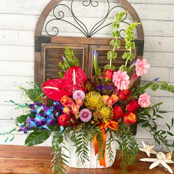 Colorful mixed flower arrangement in a white container with an orange ribbon