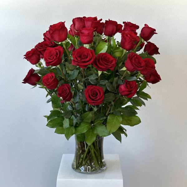 Tall arrangement of long-stemmed red roses in a clear glass vase