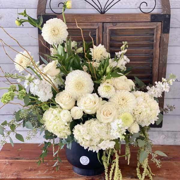 Cream floral arrangement in a dark vase with roses, dahlias, and hydrangeas