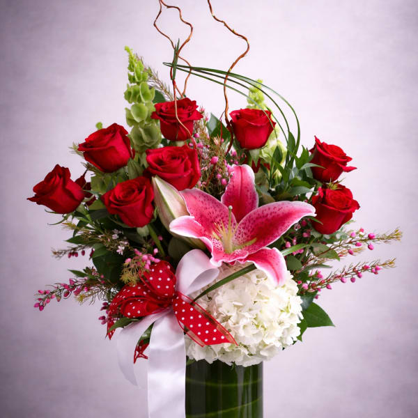 Red roses and a pink lily in a tall glass vase with ribbon