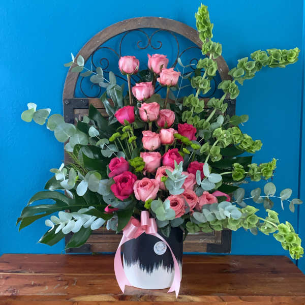 Pink rose arrangement in a white vase with a pink ribbon