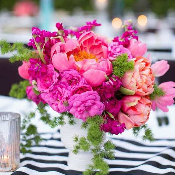 Pink and coral flowers arranged in a white vase on a striped tablecloth.