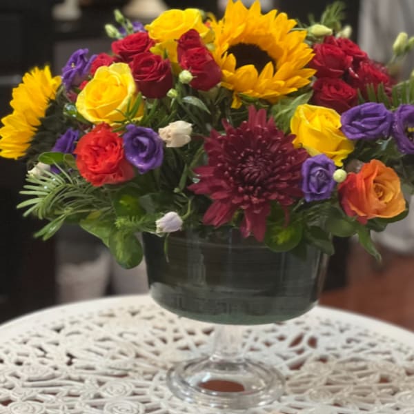Mixed bouquet of roses, sunflowers, and chrysanthemums in a glass vase