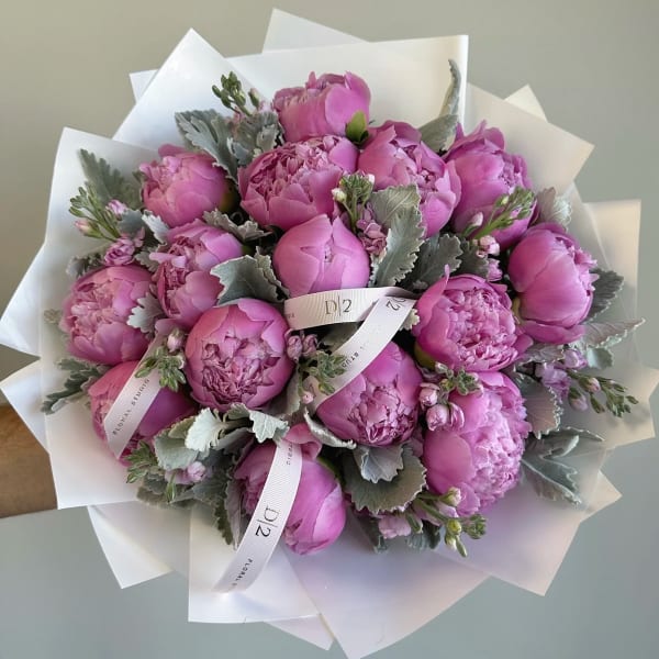 Pink peony bouquet wrapped in white paper with a ribbon
