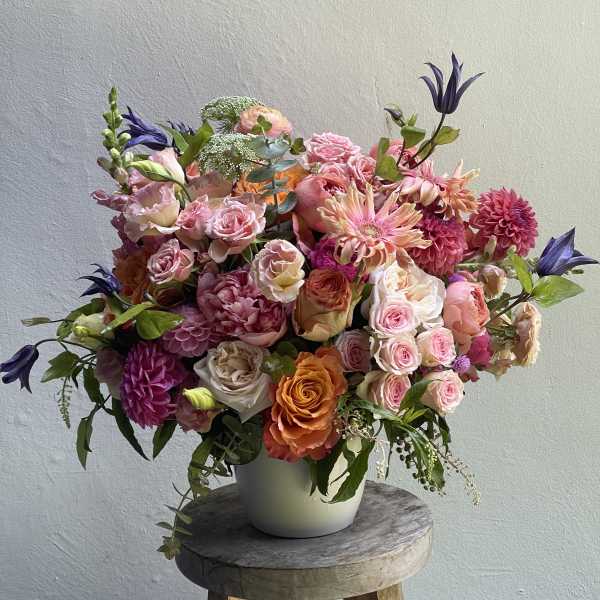 Large mixed bouquet of pink, peach, and purple flowers in a white vase