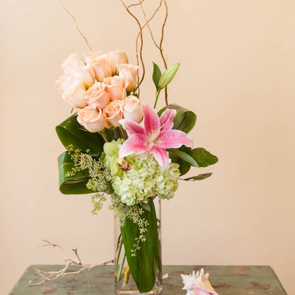 Tall bouquet of peach roses and pink lily in a glass vase