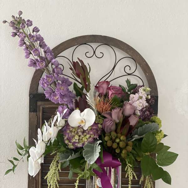 Purple and white floral arrangement in a tall silver vase