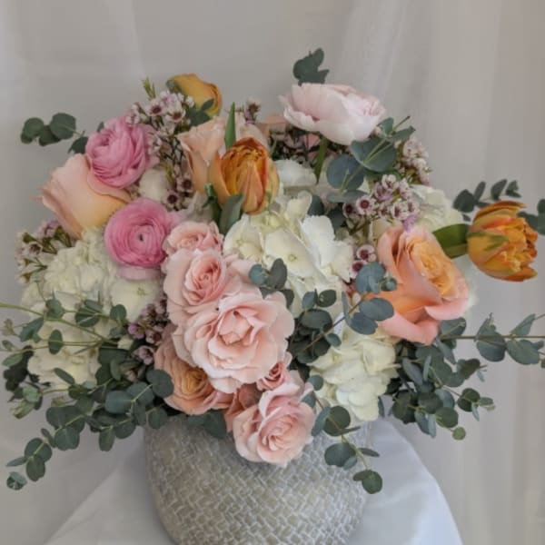 Round arrangement of blush roses, white hydrangeas and pink ranunculus in a textured gray ceramic vase