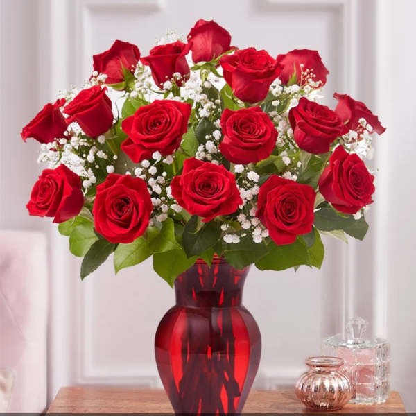 Red roses arranged in a red glass vase with white baby's breath