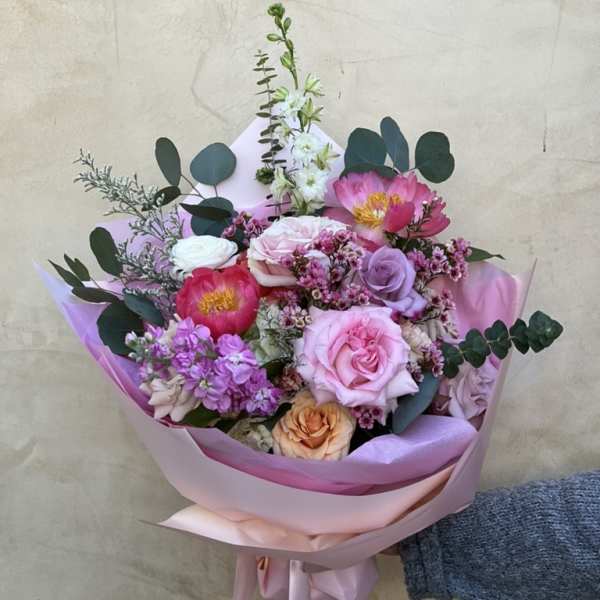 Hand-tied bouquet of pink, lavender, and peach flowers wrapped in pink paper