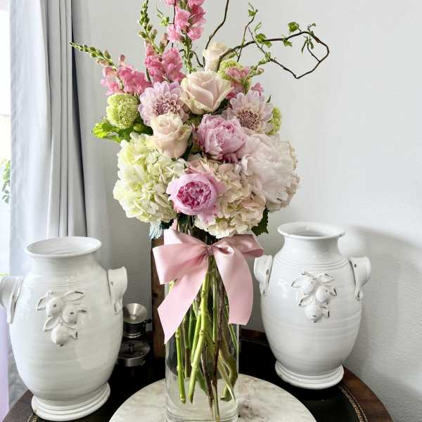 Tall pink and white floral arrangement in a clear glass vase with a pink ribbon
