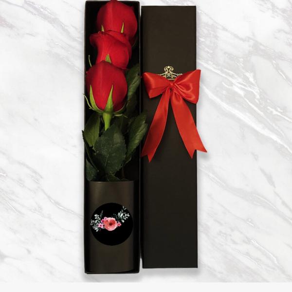 Three red roses in a black gift box with a red ribbon