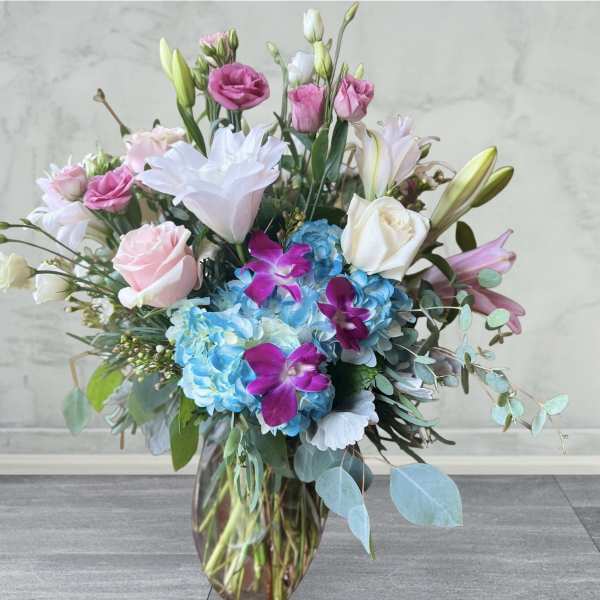 Mixed bouquet of pink, white, and blue flowers in a glass vase