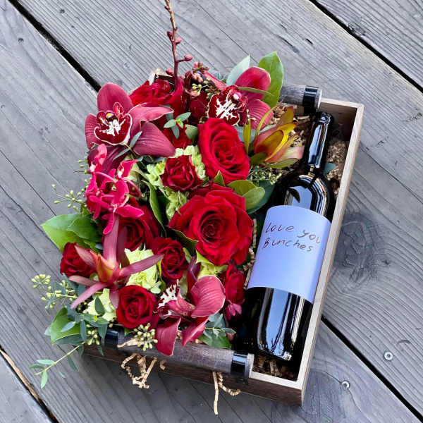 Red rose and orchid arrangement in a wooden box with a wine bottle