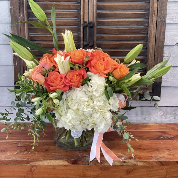 Bouquet of orange roses, white hydrangeas, and lilies in a glass vase