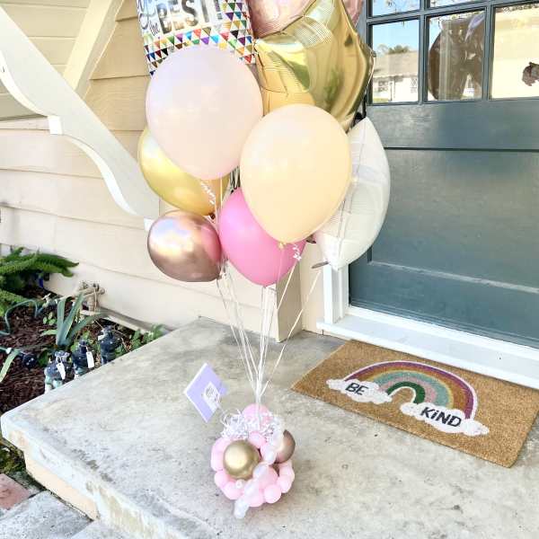 Cluster of pastel balloons with a "You're the Best" balloon and heart shapes by a front door