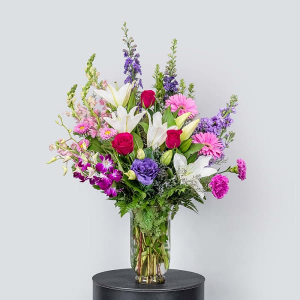 Mixed bouquet of lilies, roses, and purple flowers in a glass vase