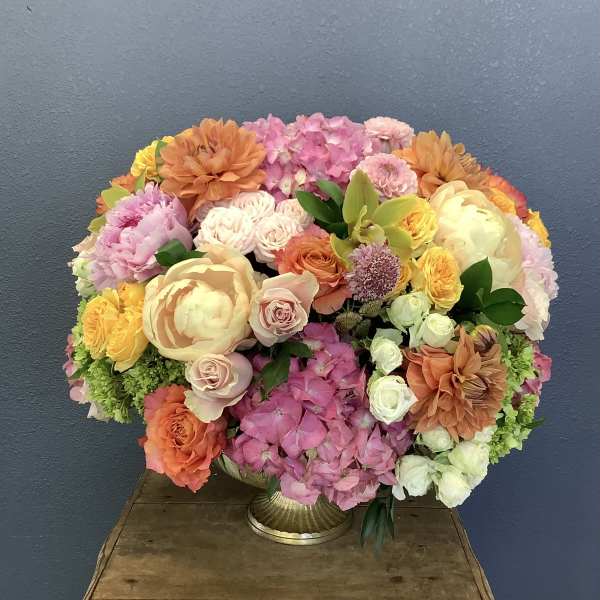 Large mixed bouquet in a gold vase with pink, peach, yellow, and white blooms