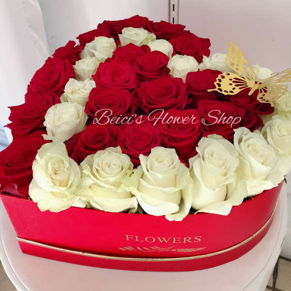 Red and white roses arranged in a heart-shaped box with a butterfly decoration