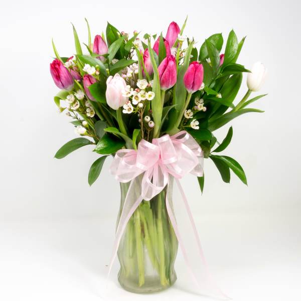 Pink and white tulip bouquet in a glass vase with a pink ribbon