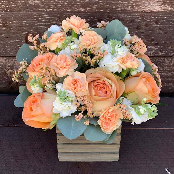 Peach roses and carnations in a wooden box with pale blue flowers