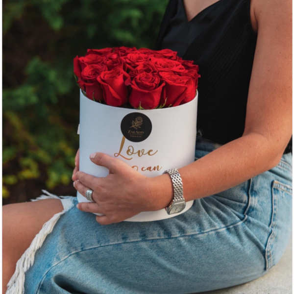 Red roses arranged in a white round box held in a person's lap