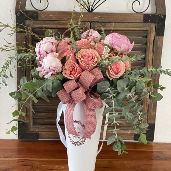 Pink roses and peonies arranged in a white vase with a ribbon
