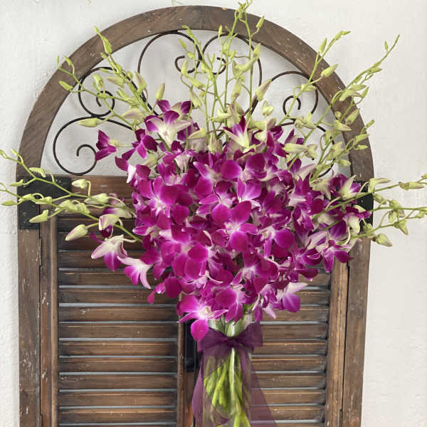 Purple orchids arranged in a tall glass vase with a ribbon.