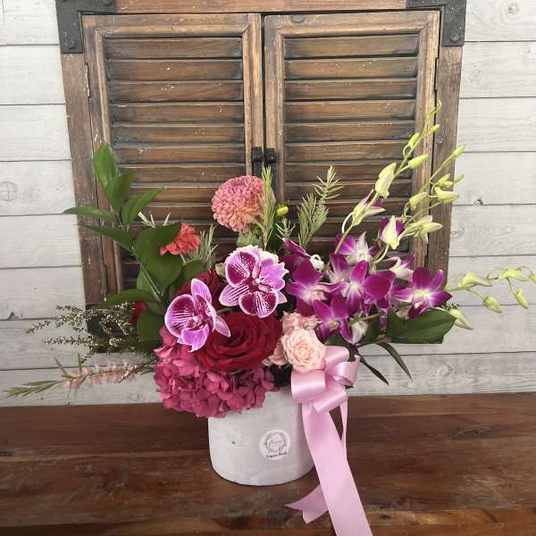 Pink and purple floral arrangement in a white vase with a pink ribbon
