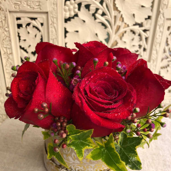 Red roses in a decorative round container with ivy accents