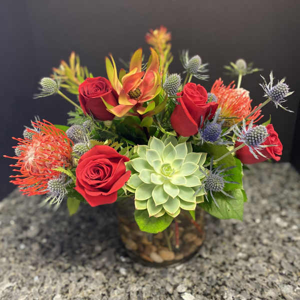 Red roses and a green succulent in a glass vase with spiky accent flowers